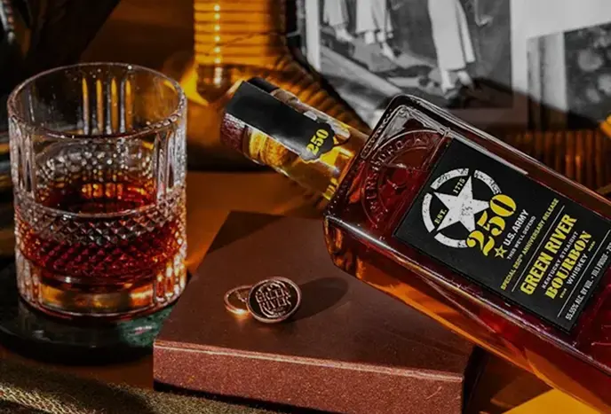 Bourbon whiskey bottle next to crystal glass with ice on wooden surface with photos