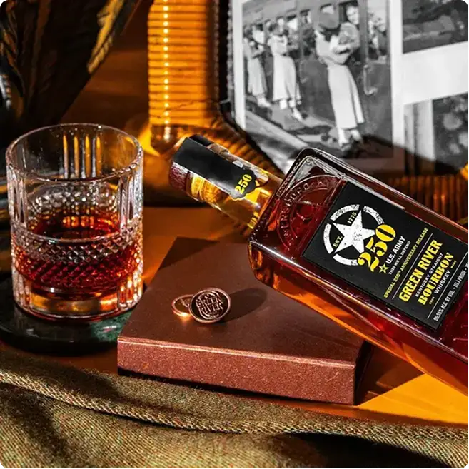 Bourbon whiskey bottle with crystal glass of amber liquid, vintage photos, and brass decor on wooden surface