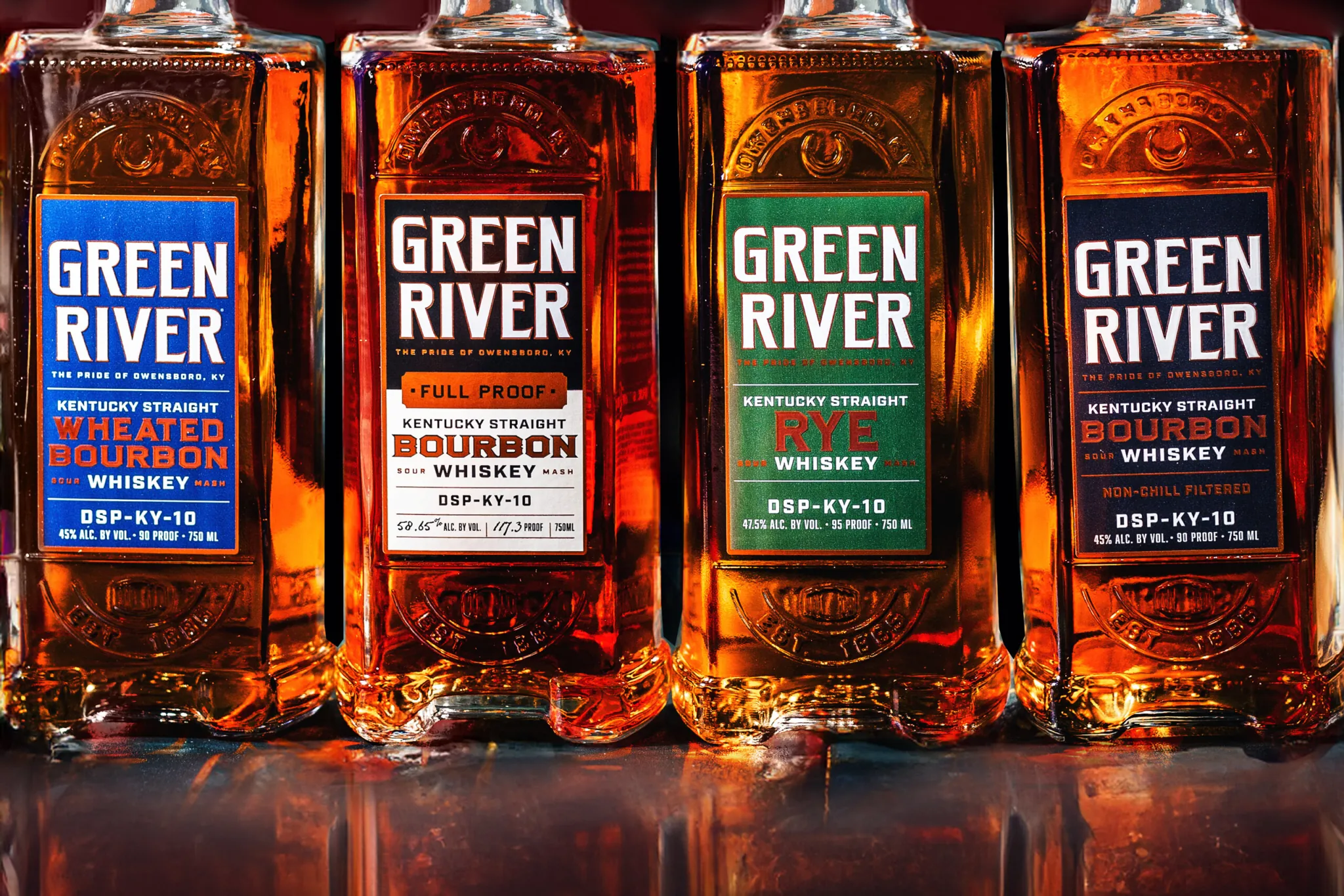Four Green River Kentucky Straight Bourbon Whiskey bottles with colored labels lined up on reflective surface.