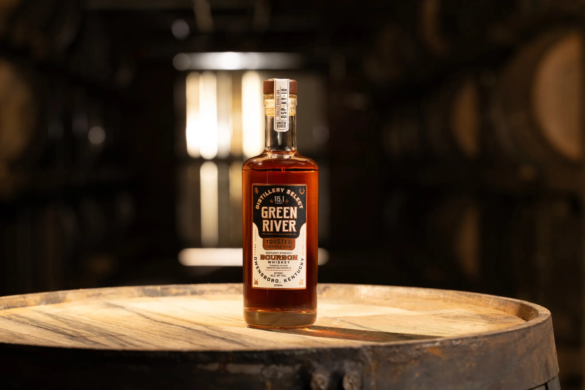 Green River bourbon whiskey bottle displayed on a wooden barrel in a distillery setting