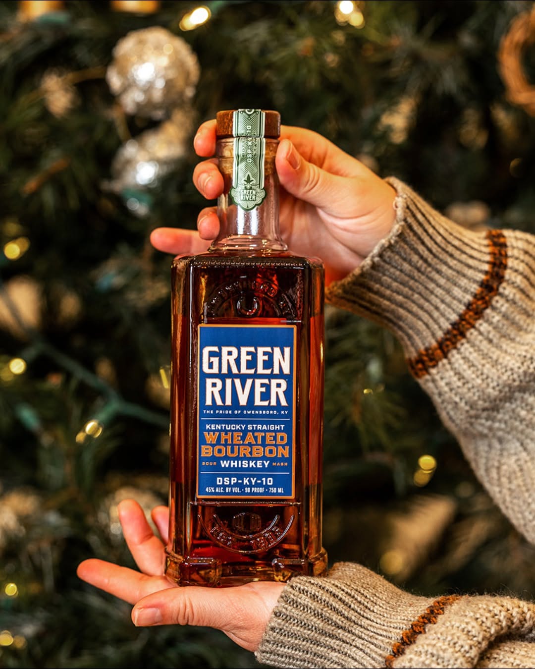 Hand holding Green River Kentucky Straight Wheated Bourbon Whiskey bottle with holiday lights in background